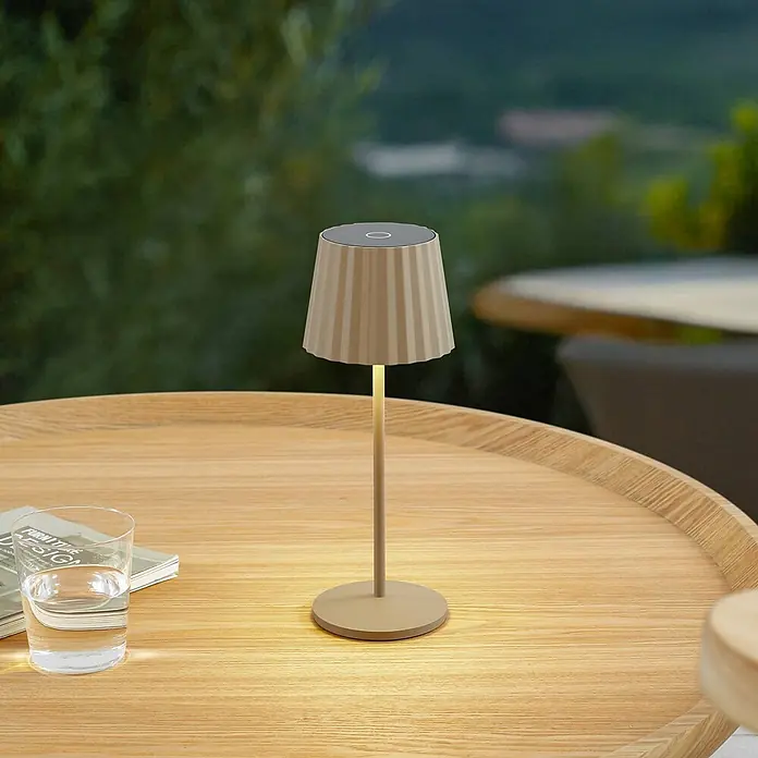 Lindby Tischleuchte Esali - creme / amber, creme / amber - Eine kleine, tragbare beige Tischlampe mit plissiertem Schirm beleuchtet einen Holztisch im Freien.