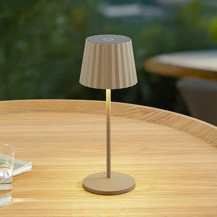 Lindby Tischleuchte Esali - creme / amber, creme / amber - Moderne beigefarbene Plissee-Tischleuchte mit dunkler Oberseite, die einen hellen Holztisch beleuchtet.