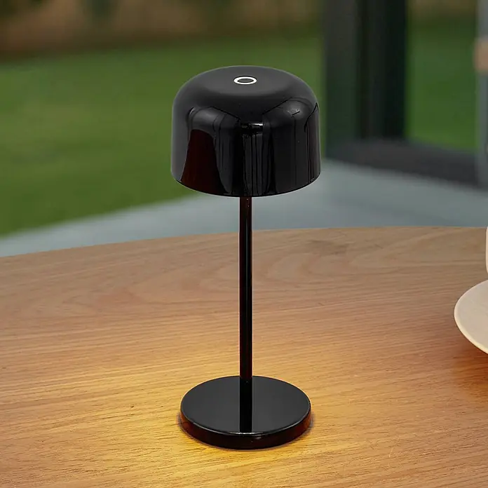Lucande Tischleuchte Quill - schwarz, schwarz - Eine schwarze, minimalistische tragbare Tischlampe beleuchtet einen Holztisch.