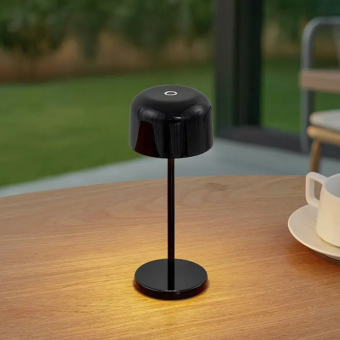 Lucande Tischleuchte Quill - schwarz, schwarz - Elegante schwarze tragbare Tischlampe auf Holzoberfläche, die warmes Licht ausstrahlt.