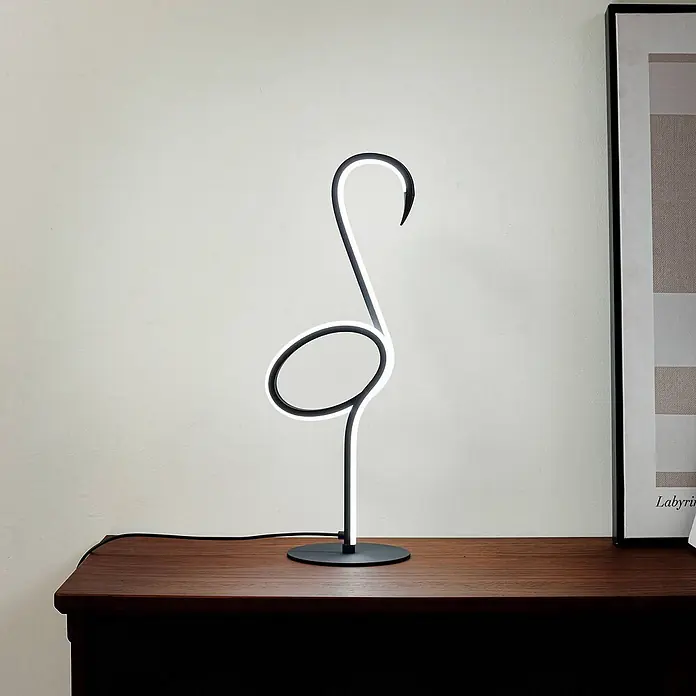 Lindby Tischleuchte Pajaro - L x B x H: 18 x 2,4 x 49,5 cm, schwarz, schwarz - Eine schwarze Flamingo-Tischleuchte mit weißem LED-Licht steht auf einem dunklen Holztisch neben einem gerahmten Bild. Das Design ist minimalistisch.