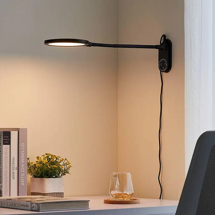 Lindby Tischleuchte Valtaria - schwarz, schwarz - Schlanke, schwarze Wand-Schreibtischlampe mit ovalem LED-Kopf und verstellbarem Arm, beleuchtet einen Arbeitsbereich.