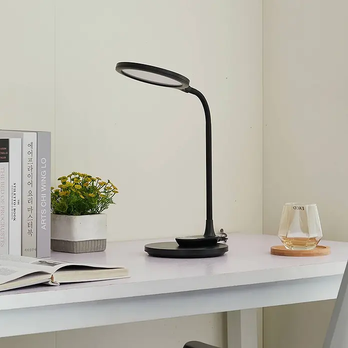 Lindby Tischleuchte Valtaria - schwarz, schwarz - Schwarze LED-Schreibtischlampe mit rundem Kopf und flexiblem Schwanenhals, leuchtet einen weißen Schreibtisch aus.