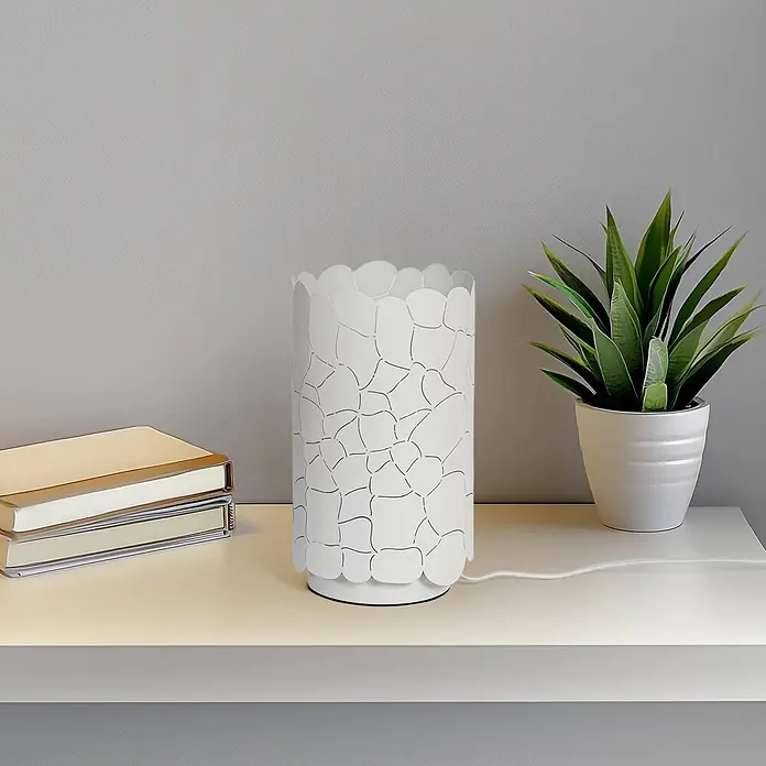 Lindby Tischleuchte Aralena - weiß / opal, E27 - Weiße zylindrische Tischleuchte mit filigranem Ausschnittmuster am Schirm, auf einem Regal mit Büchern und einer Pflanze.