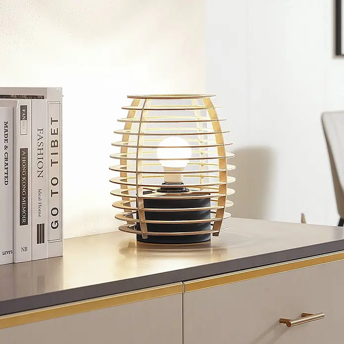 Lindby Tischleuchte Ediz - L x B x H: 22 x 22 x 25 cm, Holz hell, E27 - Eine Tischleuchte mit Holzlamellenschirm und schwarzem Sockel beleuchtet eine Kommode neben Büchern.