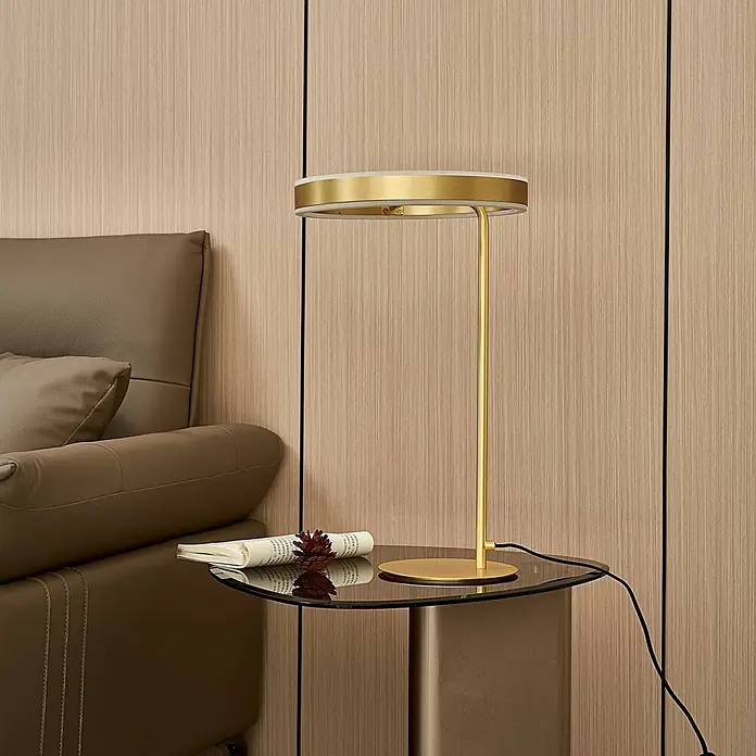 Lucande Tischleuchte Yekta - L x B x H: 30 x 30 x 58,5 cm, messing / gold, messing / gold - Goldfarbene Metall-Tischlampe mit rundem Kopf und Fuß, auf einem Glastisch neben einem braunen Sessel platziert.