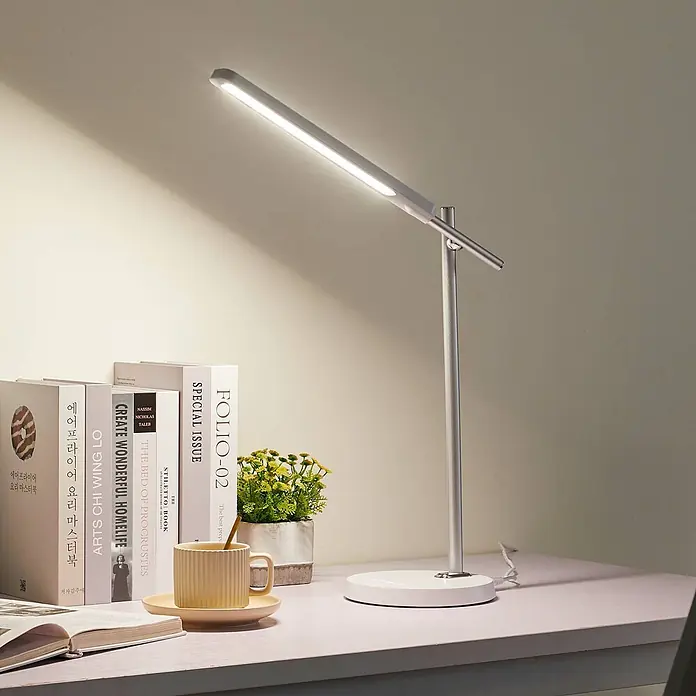 Lindby Tischleuchte Valtorin - weiß / opal, weiß / opal - Moderne silberne Schreibtischlampe mit linearem LED-Kopf, beleuchtet einen hellen Schreibtisch mit Büchern und Tasse.