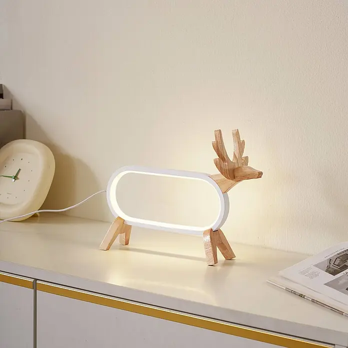 Lindby Tischleuchte Hirvi - L x B x H: 31 x 10 x 23 cm, Holz hell, weiß / opal - Eine hölzerne Hirsch-Tischlampe mit weißem, beleuchtetem Ovalkörper steht auf einem hellen Schrank.