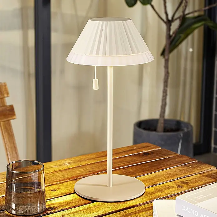 Lindby Tischleuchte Ilvi - L x B x H: 17,5 x 17,5 x 35 cm, creme / amber, creme / amber - Cremefarbene, tragbare Tischlampe mit plissiertem Stoffschirm und Zugschalter auf einem Holztisch.