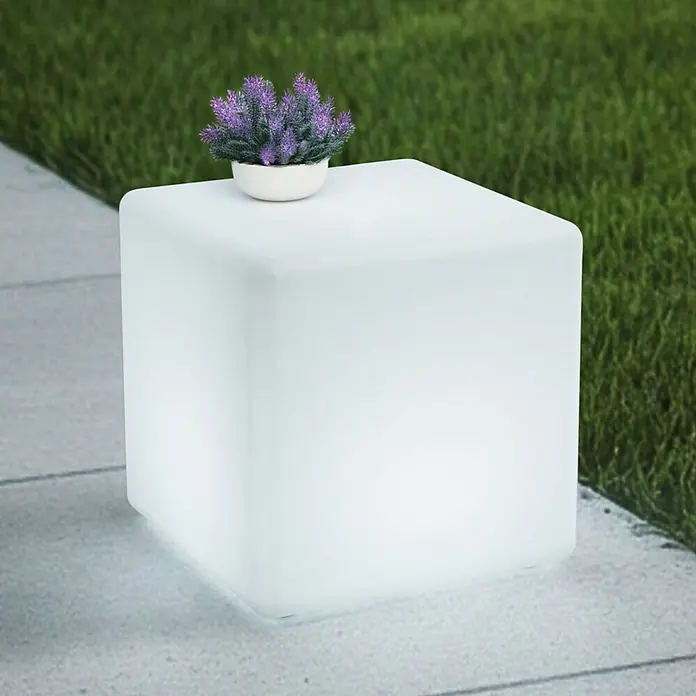 Lindby Tischleuchte Cubara - weiß / opal - Weißer leuchtender Outdoor-Würfeltisch mit einer lila Topfpflanze.