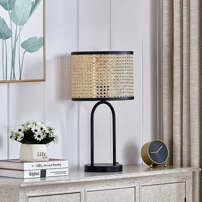 Lindby Tischleuchte Yaelle - Holz hell, E27 - Schwarze Metall-Tischleuchte mit natürlichem Rattan-Schirm auf einer Holzkommode.