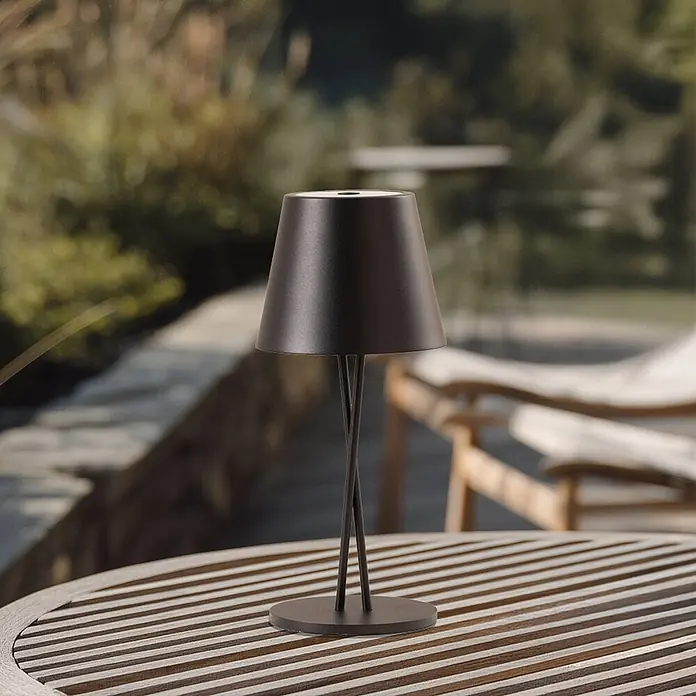 Lindby Tischleuchte Janea - L x B x H: 11,4 x 11,4 x 25 cm, schwarz, schwarz - Schwarze tragbare Außenleuchte mit konischem Schirm auf einem gelatteten Holztisch.