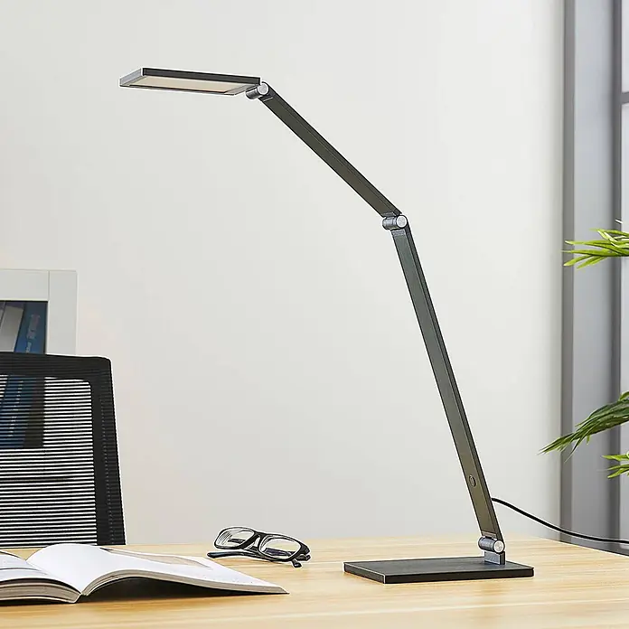 Lucande Tischleuchte Mion - L x B x H: 36,5 x 12 x 41 cm, alu / grau / zink, alu / grau / zink - Moderne dunkelgraue, verstellbare LED-Schreibtischlampe auf einem Holzschreibtisch neben einem offenen Buch und einer Brille.