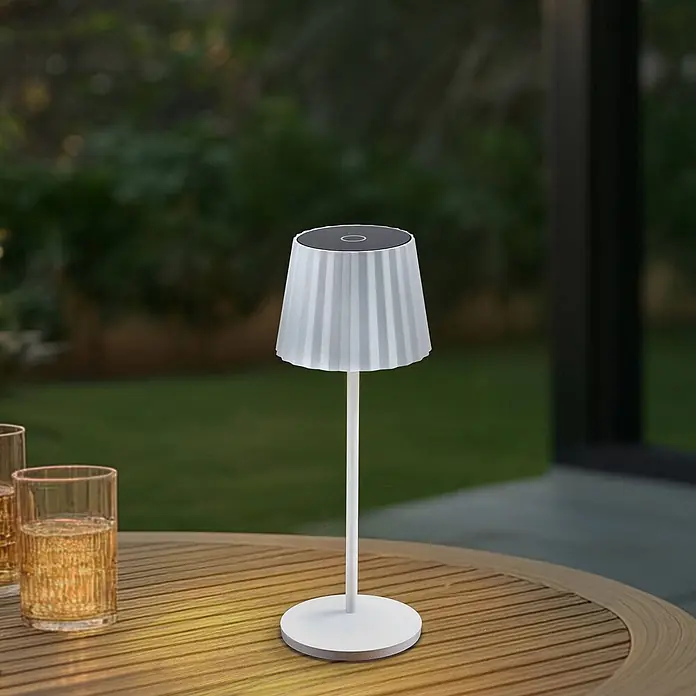 Lindby Tischleuchte Esali - L x B x H: 11 x 11 x 28,5 cm, weiß / opal, weiß / opal - Weiße, tragbare Tischlampe mit geripptem Schirm auf einem Holztisch im Freien, die warmes Licht wirft.