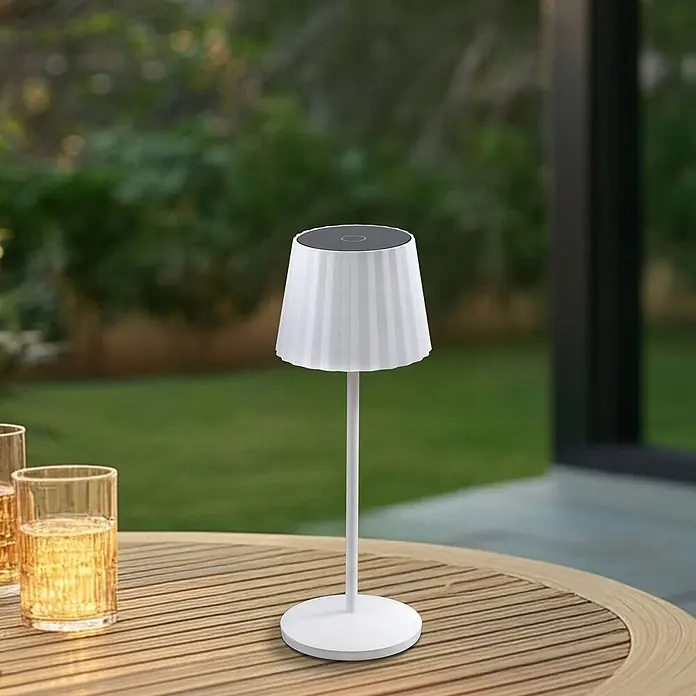 Lindby Tischleuchte Esali - L x B x H: 11 x 11 x 28,5 cm, weiß / opal, weiß / opal - Weiße tragbare Tischlampe mit plissiertem Schirm und dunkler Oberseite, auf einem Lamellen-Holztisch im Freien.