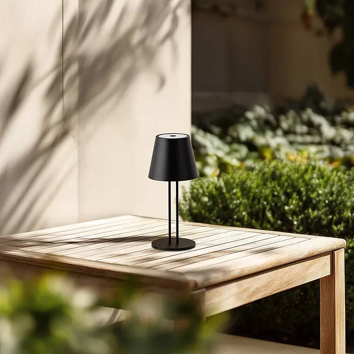 Lindby Tischleuchte Janea - L x B x H: 11,4 x 11,4 x 25 cm, schwarz, schwarz - Mattschwarze tragbare Tischlampe mit kegelförmigem Schirm auf einem Holztisch im Freien.
