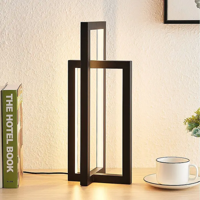 Lucande Tischleuchte Hylda - schwarz, schwarz - Moderne schwarze LED-Tischleuchte mit geometrischem Design, die einen Holzschreibtisch beleuchtet.