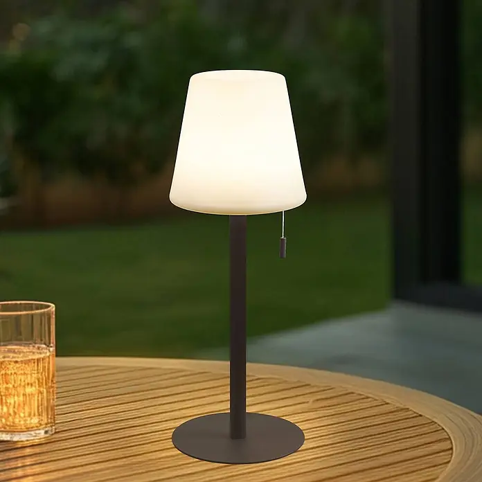 Lindby Tischleuchte Azalea - L x B x H: 16,5 x 16,5 x 45 cm, braun / rost - Kabellose Outdoor-Tischlampe mit weißem Schirm und dunkelgrauem Fuß, die einen Holztisch beleuchtet.