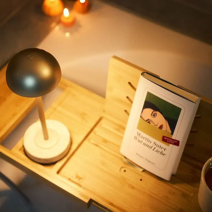 Lindby Tischleuchte Pippin - messing / gold, messing / gold - Kleine moderne Lampe mit dunklem, kugelförmigem Kopf und hellem Sockel, spendet Umgebungslicht auf einer Holz-Badewannenablage zum Lesen.