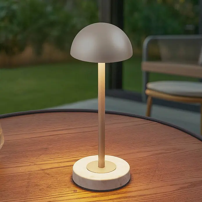 Lindby Tischleuchte Pippin - messing / gold, messing / gold - Moderne Pilz-Tischlampe mit beigem Schirm, goldenem Stiel und hellem Sockel, warm leuchtend auf einem Holztisch.