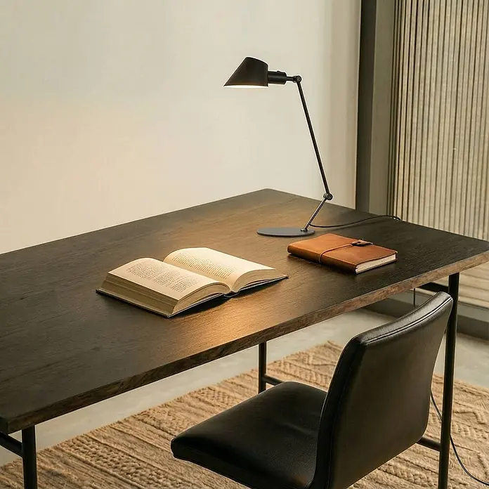 Lindby Tischleuchte Corali - schwarz, schwarz, E27 - Verstellbare Schreibtischlampe aus schwarzem Metall auf einem dunklen Holztisch, die ein offenes Buch und ein braunes Notizbuch beleuchtet.