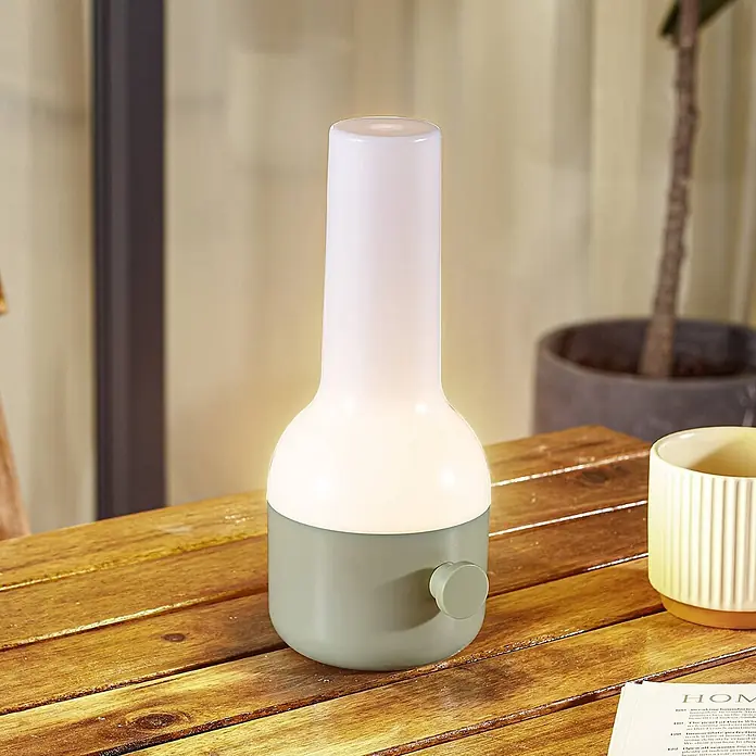 Lindby Tischleuchte Isaline - grün, weiß / opal - Eine hellgrün-weiße moderne Tischlampe mit Drehknopf an der Basis, die einen Holztisch beleuchtet.