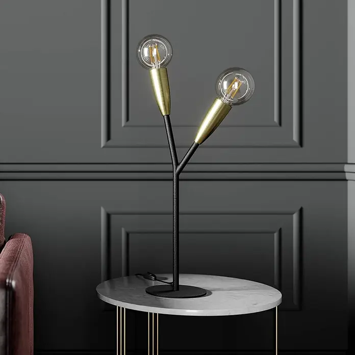 Lucande Tischleuchte Carlea - L x B x H: 23 x 23 x 59 cm, schwarz, E27 - Eine moderne Tischlampe mit schwarzem Y-förmigem Ständer und messingfarbenen Fassungen mit zwei klaren Glühbirnen, auf einem Marmor-Beistelltisch platziert.