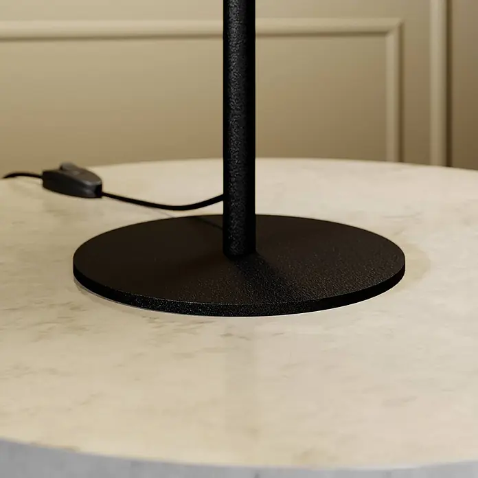 Lucande Tischleuchte Carlea - L x B x H: 23 x 23 x 59 cm, schwarz, E27 - Schwarzer, strukturierter Metallsockel einer Lampe mit Stiel und Netzkabel auf einem hellen Marmortisch.