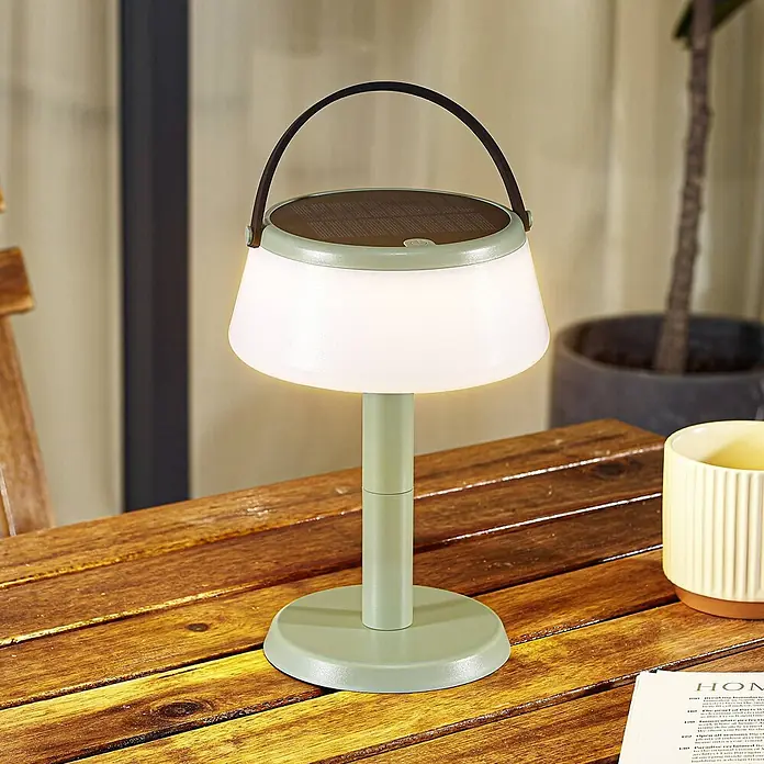 Lindby Tischleuchte Mikkel - L x B x H: 14,2 x 14,2 x 7,2 cm, grün - Eine hellgrüne solarbetriebene LED-Tischleuchte mit weißem Diffusor und dunklem Griff, auf einem Holztisch stehend.