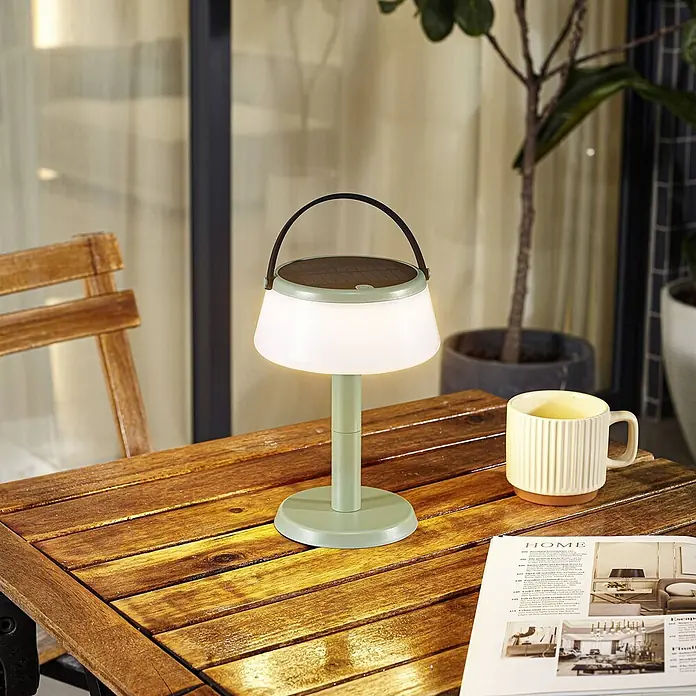 Lindby Tischleuchte Mikkel - L x B x H: 14,2 x 14,2 x 7,2 cm, grün - Mintgrüne Solartischlampe mit weißem Diffusor und dunklem Griff auf einem Holztisch, warm leuchtend.