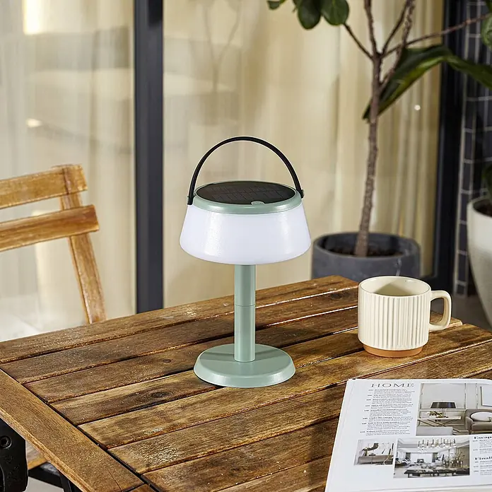 Lindby Tischleuchte Mikkel - L x B x H: 14,2 x 14,2 x 7,2 cm, grün - Hellgrüne und weiße Solartischlampe mit schwarzem Griff auf einem hölzernen Gartentisch.