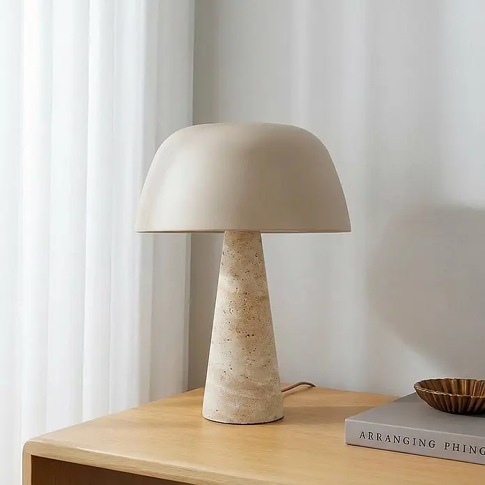 Lindby Tischleuchte Magritt - creme / amber, creme / amber, E27 - Pilz-Tischlampe mit cremefarbenem Schirm und strukturierter Travertin-Basis auf einem Holztisch.