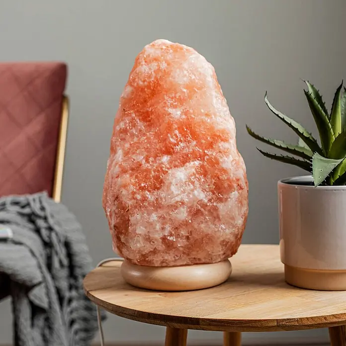 Envostar Tischleuchte Harmony - rot, E14 - Eine pinkfarbene Himalaya-Salzlampe mit natürlicher, rauer Textur und Holzsockel auf einem Holztisch in einem gemütlichen Raum.