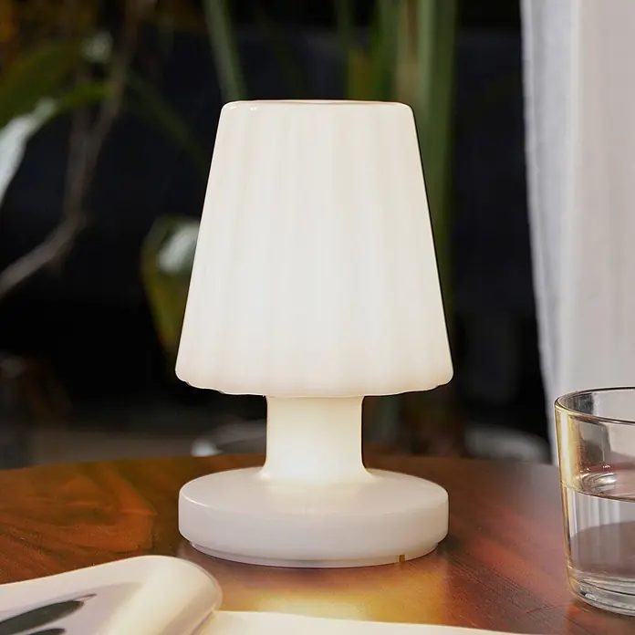 Lindby Tischleuchte Jovem - weiß / opal, weiß / opal - Eine leuchtende, weiße Tischlampe mit geripptem Schirm auf einem Holztisch.