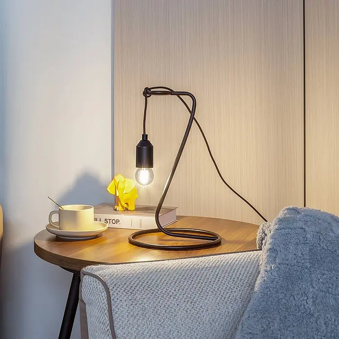 Lindby Tischleuchte Elira - schwarz, schwarz, E27 - Moderne schwarze Metall-Tischlampe mit Glühbirne, beleuchtet einen Beistelltisch neben einem gemütlichen Sofa.