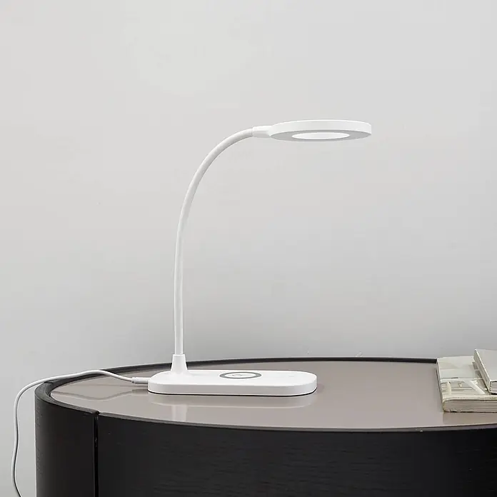 Lindby Tischleuchte Siona - weiß / opal, weiß / opal - Weiße flexible LED-Schreibtischlampe mit rundem Leuchtkopf und Basis mit kabelloser Ladefunktion, auf einem Tisch.