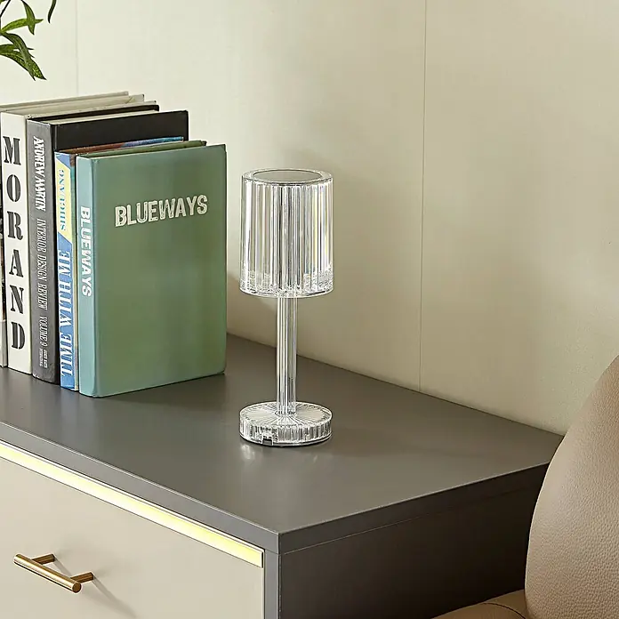 Lindby Tischleuchte Louane - L x B x H: 8,5 x 8,5 x 25,7 cm, klar / transparent, klar / transparent - Transparente, gerillte Tischlampe auf einem Schreibtisch neben Büchern.