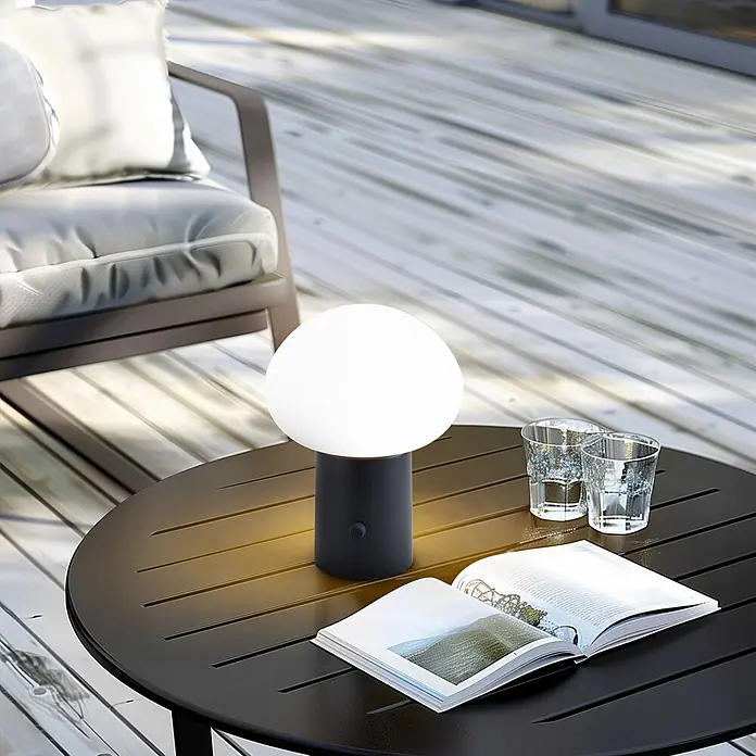 Lindby Tischleuchte Zelie - schwarz, weiß / opal - Schwarze, tragbare Tischleuchte mit weißem kugelförmigem Diffusor, die ein offenes Buch auf einem Gartentisch beleuchtet.