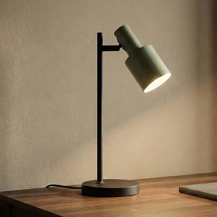 Lindby Tischleuchte Ovelia - schwarz, grün, E27 - Dunkelgrüne und schwarze Schreibtischlampe auf einem Holzschreibtisch, die warmes Licht spendet.