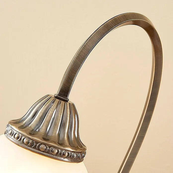 Lindby Tischleuchte Mialina - bronze / altmessing, E27 - Geschwungener Arm einer Lampe aus antikem Messing, der aus einem geriffelten Fuß ragt und einen leuchtenden weißen Glasschirm hält.