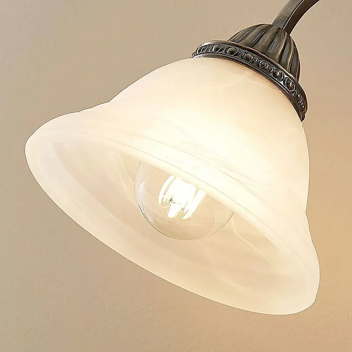 Lindby Tischleuchte Mialina - bronze / altmessing, E27 - Glockenförmige Lampe mit weißem, gewirbeltem Glasschirm, glühender klarer Glühbirne und antikbronzenem Beschlag.