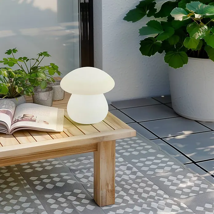Lindby Tischleuchte Vernate - weiß / opal, weiß / opal - Eine matte, weiße pilzförmige Außenleuchte auf einem hellen Holztisch, die für stimmungsvolle Beleuchtung auf einem Balkon sorgt.