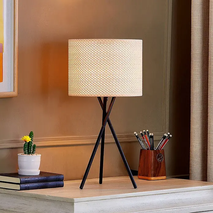 Lindby Tischleuchte Soula - L x B x H: 26 x 26 x 52 cm, schwarz, creme / amber, E27 - Zylindrische Tischleuchte mit beigem Stoffschirm und schwarzem Dreibeinfuß auf hellem Schreibtisch.