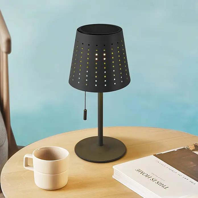 Lindby Tischleuchte Hilario - schwarz, schwarz - Schwarze Tischlampe mit perforiertem, quadratischem Schirm und Zugkette, auf einem Holztisch, wirft gemustertes Licht.