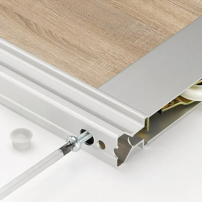 Room Plaza Easy Schiebetür-Bau-Set - Eiche geplankt/Eiche Trüffel, Farbe Beschlag: Silber - Detailaufnahme eines silbernen Schiebetürrahmens mit Schraube und Schraubendreher, hervorgehoben durch Holzboden.