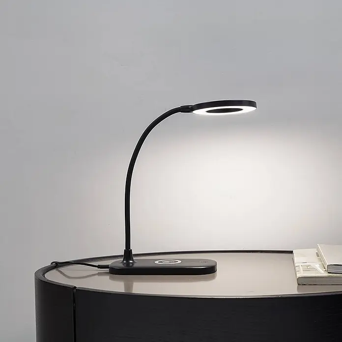Lindby Tischleuchte Siona - schwarz, schwarz - Schwarze, flexible LED-Schreibtischlampe mit rundem Kopf und kabelloser Ladefunktion, beleuchtet Bücher auf einem Tisch.