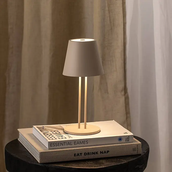 Lindby Tischleuchte Janea - creme / amber, creme / amber - Kleine Tischlampe mit grauem Kegelschirm und zwei hellen Stützen, warm leuchtend, auf Büchern auf einem dunklen Beistelltisch.