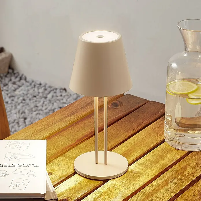 Lindby Tischleuchte Janea - creme / amber, creme / amber - Eine hellbeige Tischleuchte mit konischem Schirm und zwei Stützen auf einem Holztisch im Freien.