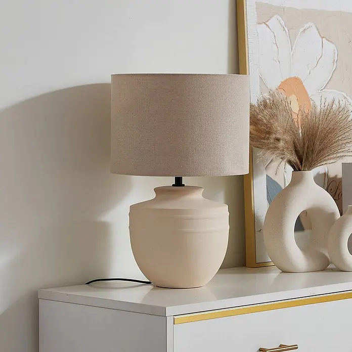 Lindby Tischleuchte Thalassia - L x B x H: 30 x 30 x 45,5 cm, creme / amber, creme / amber, E27 - Creme Keramik-Tischlampe mit beigem Leinenschirm auf einer weißen Kommode.