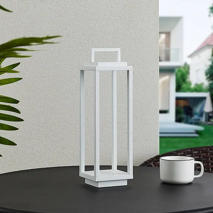 Lucande Tischleuchte Mirina - L x B x H: 10 x 10 x 33,5 cm, weiß / opal - Weiße, rechteckige Laterne auf einem dunklen Tisch neben einer Tasse, für den Außenbereich.